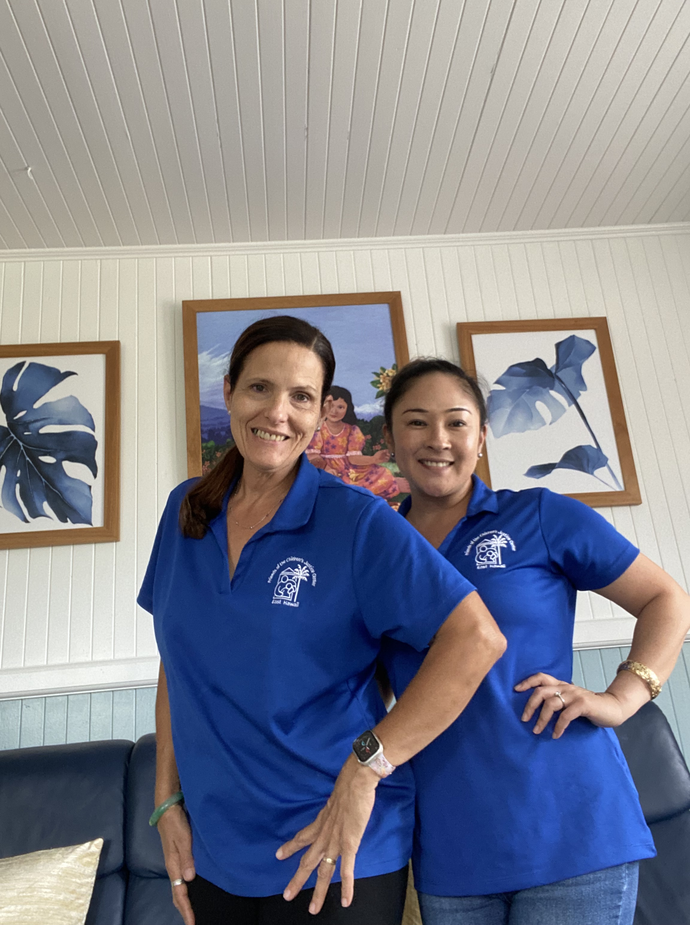 two women in blue shirts smiling in front of photos