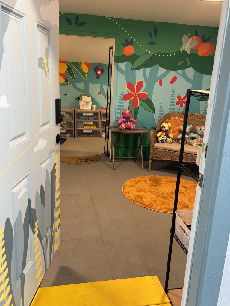 a photo of a door slightly open ajar showing a bright interior room for children with a painted mural of flowers and rainbows and plants